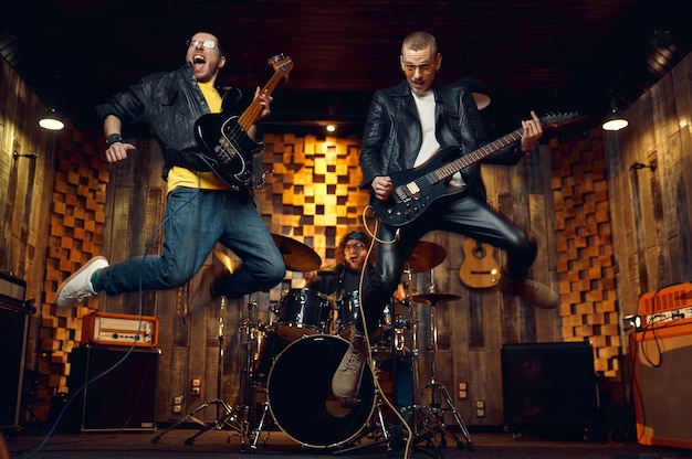 Фото Два брутальных музыканта прыгают с электрогитарой, на сцене играет музыка. выступление рок-группы или повторение в гараже, человек с музыкальным инструментом, живой звук
