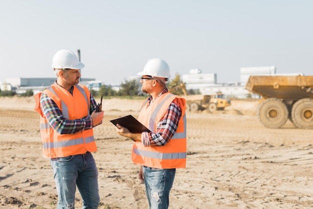 Two builders in orange vests and helmets working on the road construction field