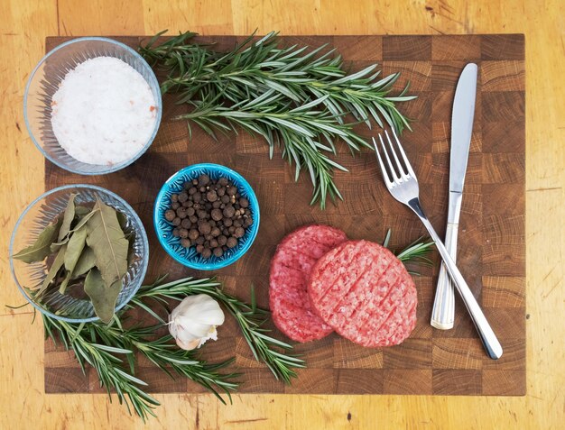 Two burger patties on a wooden board Meat with spices for cooking Garlic pepper