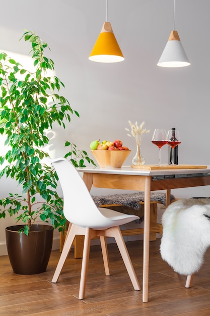 Two burgundy glasses of red wine, wooden bowl with green and red apples, decor vase on table in kitchen