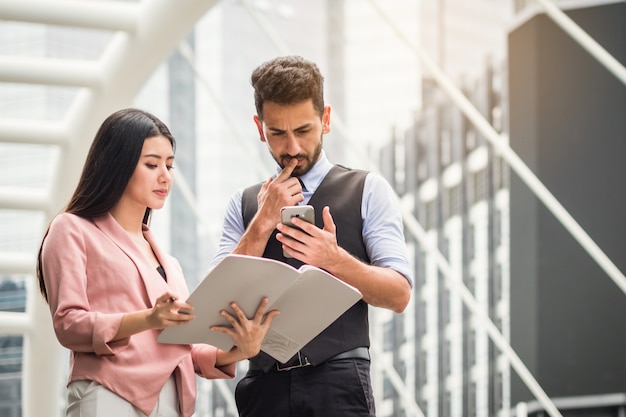 Two business analysts discussing online data in front of book board at the outside city