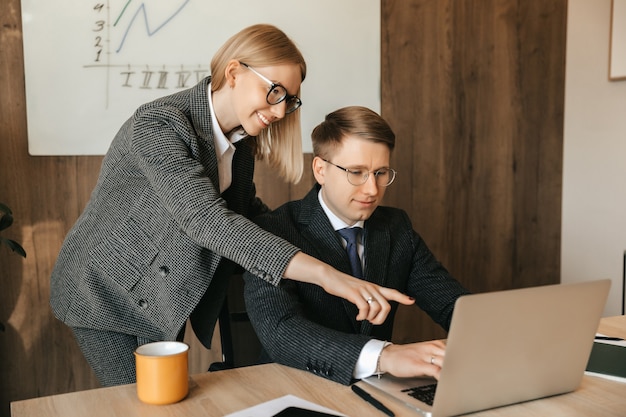 Two business colleagues look at documents and work on a laptop, secretary or woman manager reads a document, smiling businesswoman.