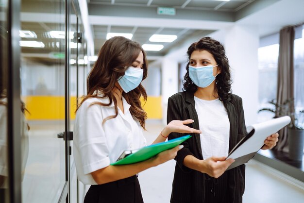 Foto due colleghi di lavoro in maschera protettiva che discutono di questioni relative al lavoro in un ufficio