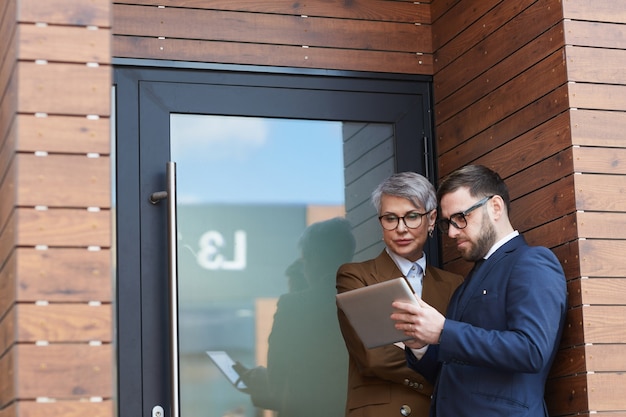 Two business colleagues using digital tablet together while standing outdoors near the office door