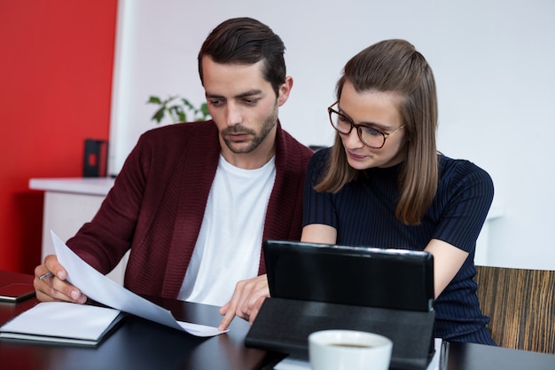 Two business executives discussing over digital tablet and document in meeting