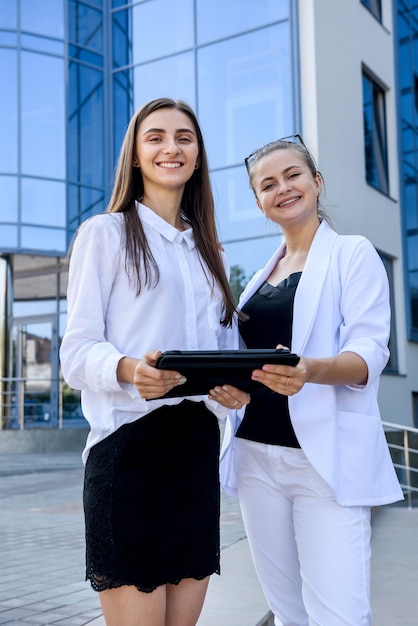 Two business ladies standing outside. one of them is very\
happy