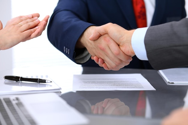 Two business man shaking hands to each other above signed contract.