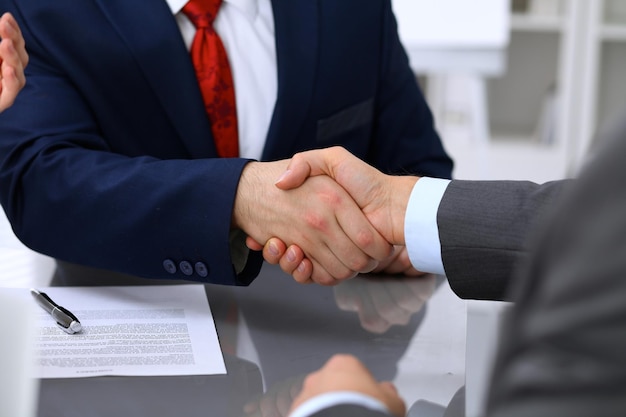 Two business man shaking hands to each other above signed contract.