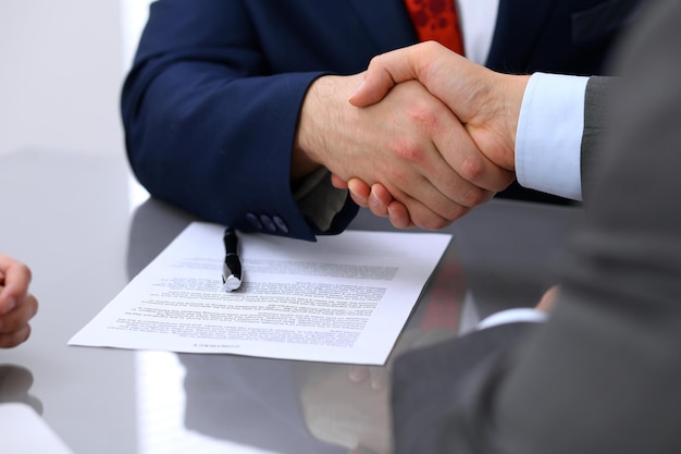 Two business man shaking hands to each other above signed contract.