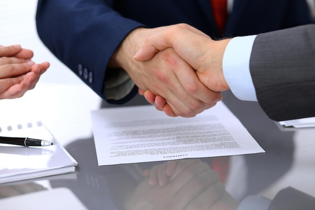 Two business man shaking hands to each other above signed contract.