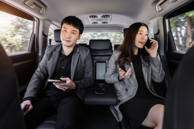 Two business man and woman using mobile phone while sitting at the back seat of a car