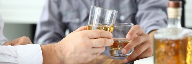 Two business men drinking cognac from glasses at workplace closeup