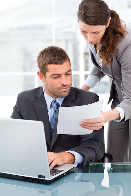 Two business people looking at a paper while working on the laptop