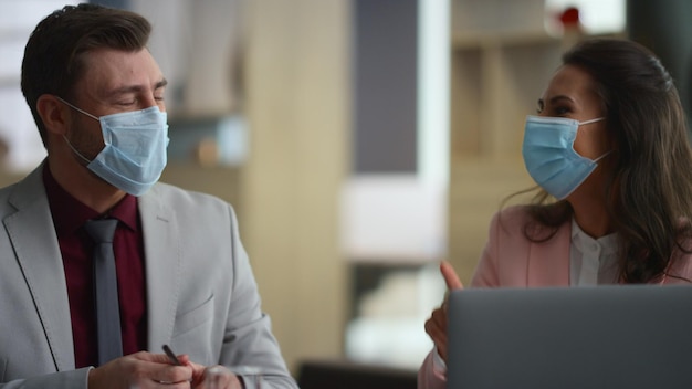 Two business people talking corporate data wearing facial covid mask in financial company office Young managers team communicate in workplace Lawyers smile laugh indoors Work conversation concept