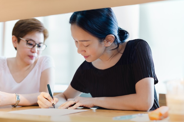 Two business woman signing contract agreement during meeting in cafe.