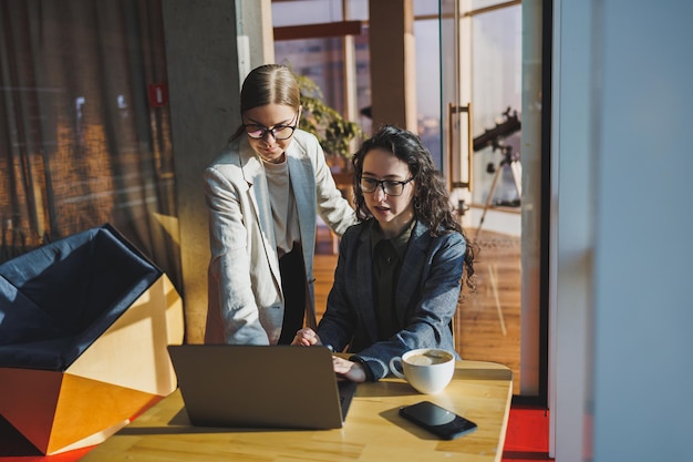 Photo two business women are looking for something in a laptop concept of business cooperation and teamwork young smiling women at the desk in the office modern successful people