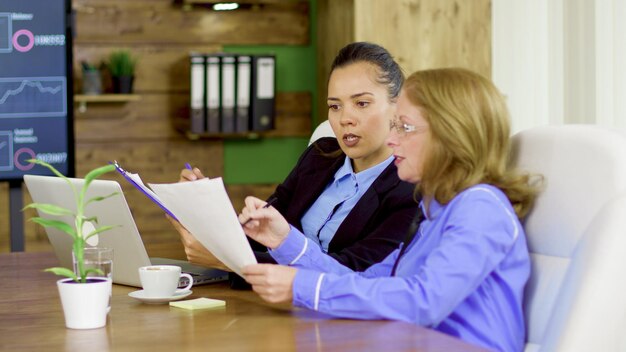 Two business women in the conference room looking at firm statistics report.