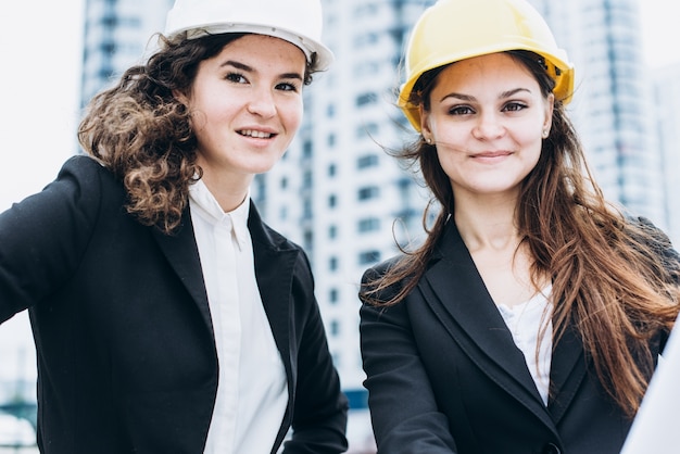 Two business women in protective helmets and safety glasses looking at building schemes, architectural concept