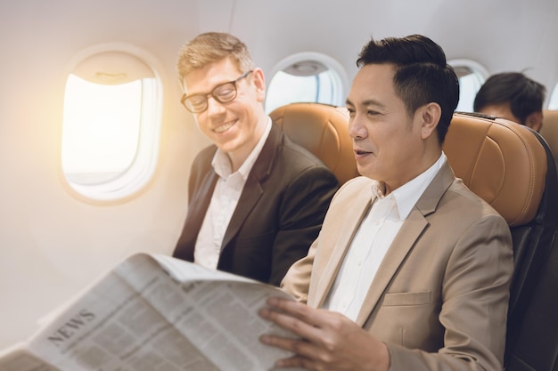 Two businessman in flight cabin talking together about news
article in news paper happy smile