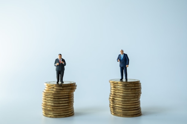 Two Businessman miniature figure people figure standing on stack of coins.