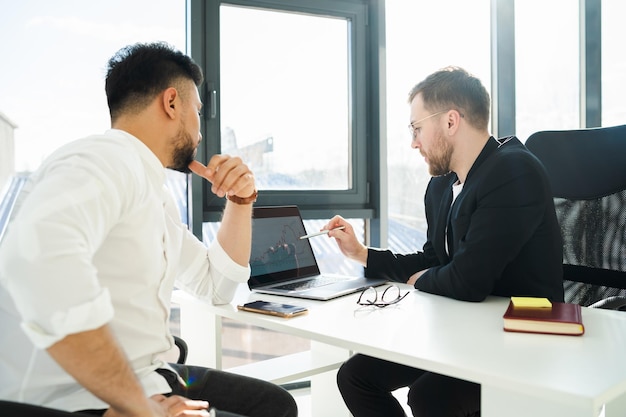 Two businessmen analyze the growth of the company sitting at the laptop in the office