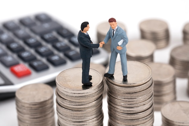 Two businessmen handshake on top of stack of coins