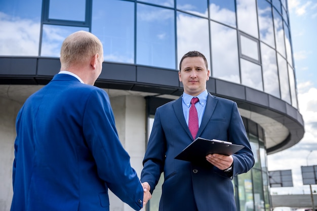 Two businessmen handshaking against new building