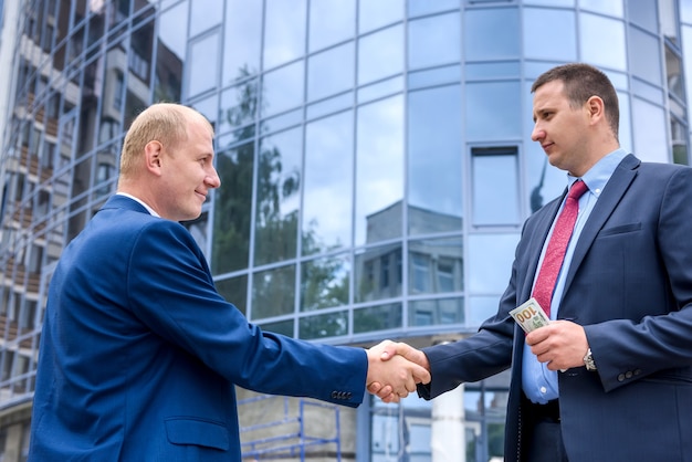 屋外の新しい建物の前に握手する2人のビジネスマン