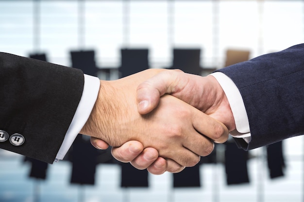 Two businessmen shake hands on the background of bright conference room investing concept close up