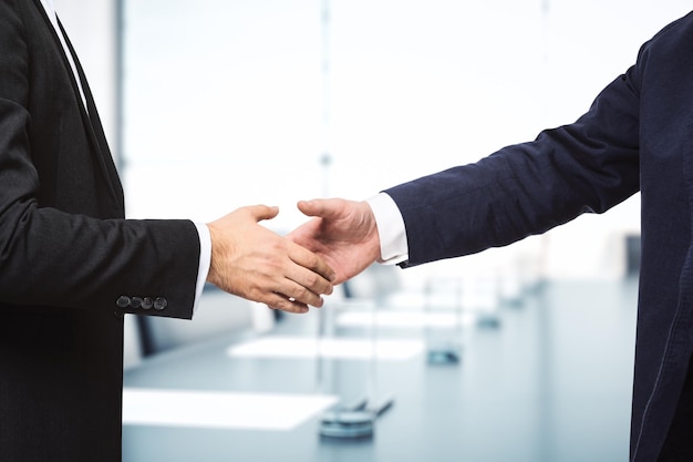 Two businessmen shake hands on the background of sunny meeting room deal concept close up