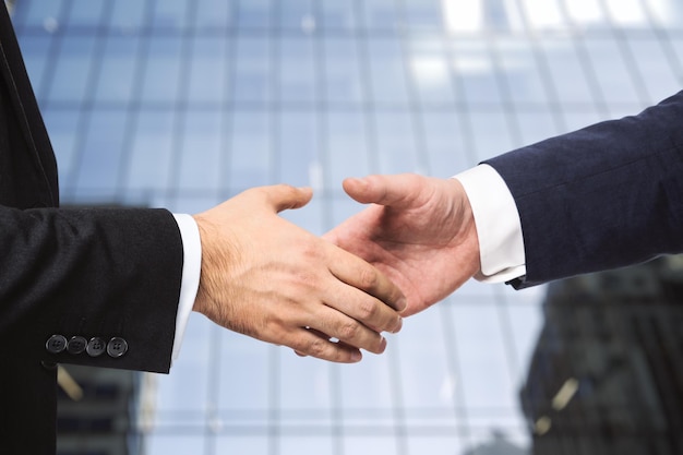 Two businessmen shake hands on office building background partnership concept closeup