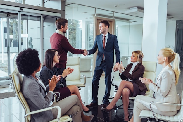 Two businessmen shaking hands in front of coworkers during a meeting