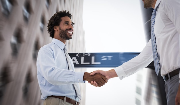 Two businessmen shaking hands in office against wall street