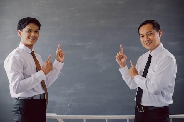 Two businessmen in shirts and ties smiling while pointing up to the empty space for business mockup