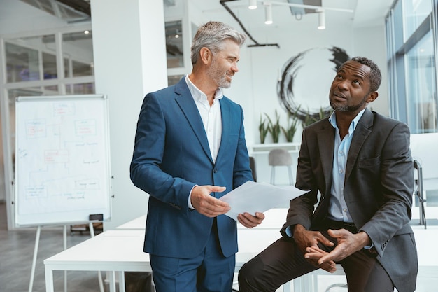 Two businessmen talking about deal standing in meeting room in modern office