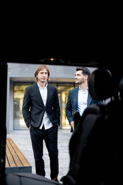 Two businessmen walk to the car from a building