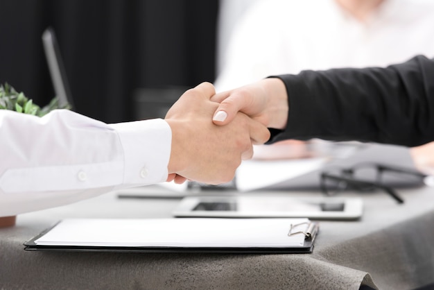 Photo two businesspeople shaking each other's hand over the clipboard on the desk