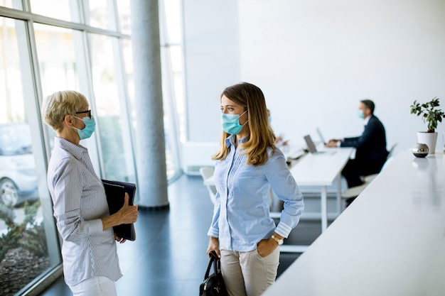 Two businesswomen, mature and young one, talking in the office and wearing mask as a virus protection