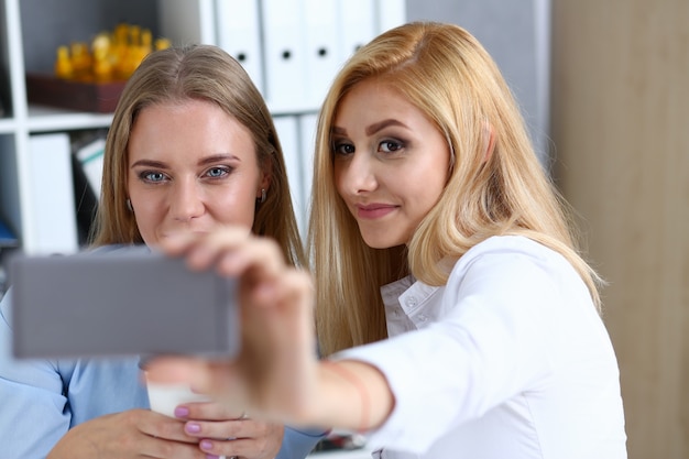 Due donne d'affari in ufficio sorridono e si fanno selfie