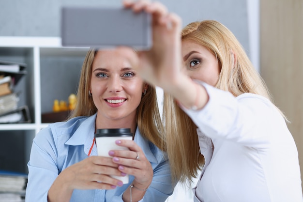 Two businesswomen in the office smile and do selfie