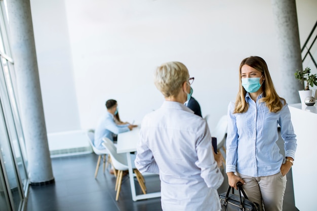 Two businesswomen talking in the office and wearing mask as a virus protection