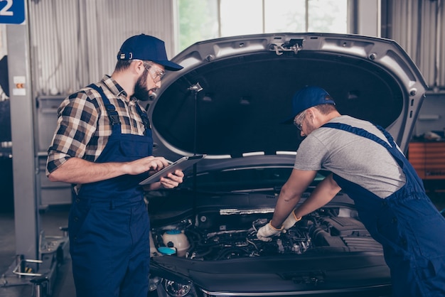 Two busy mechanical engineers experts at work shop in special blue uniform