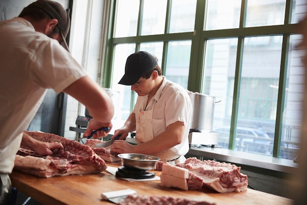 2人の肉屋が肉屋で売るために肉を切る