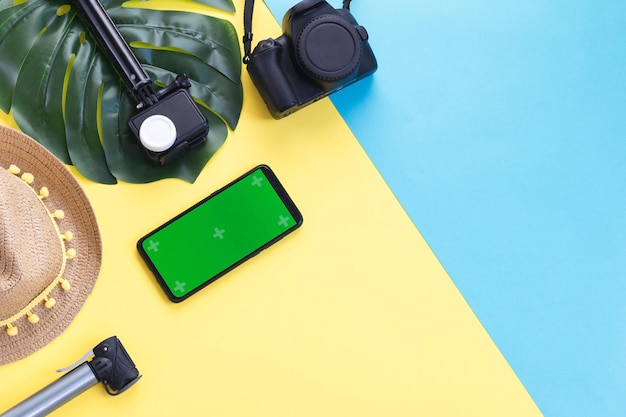 Two cameras a straw hat a manster leaf and a smartphone on a yellow background