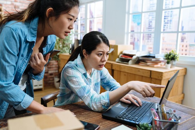 Due candide giovani donne asiatiche infelici colleghe revisore dei conti dipendente che si sentono confuse nel magazzino. ragazze colleghe faccia perplessa esprimendo dubbio incertezza con l'ordine del cliente sul laptop online.