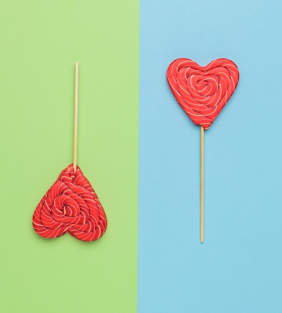 Two candies on sticks in the shape of hearts on a green and blue background Minimal concept of sweet life and love