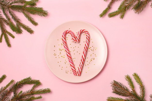 Two Candy Canes in heart shape on gold glitter stars on pink plate on light background.