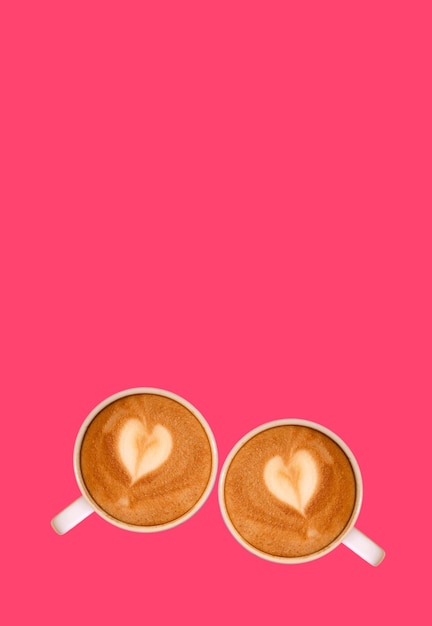 핫 핑크 배경에 하트 모양의 라떼 아트가 있는 카푸치노 커피 두 개