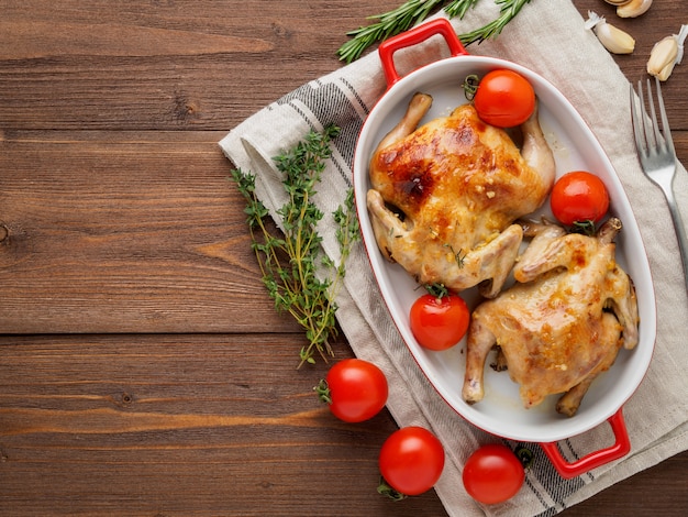 Foto due carcasse di pollo fritto in una ciotola, mandrini al forno in un forno con pomodori