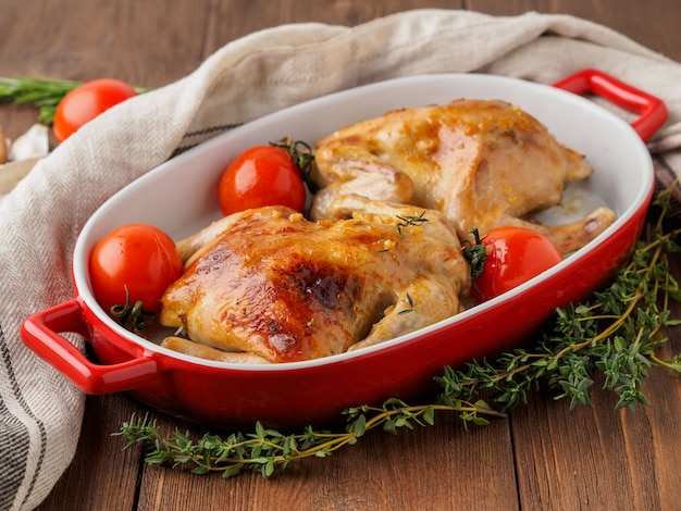 Foto due carcasse di pollo fritto in una ciotola, mandrini al forno in un forno con pomodori